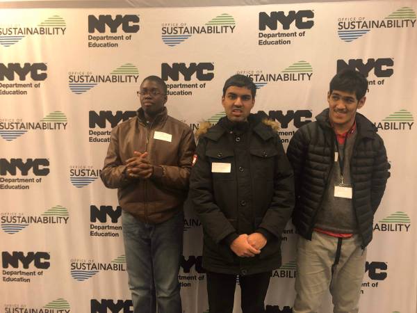 3 student from Queens Transition Center stand in front of Sustainability banner